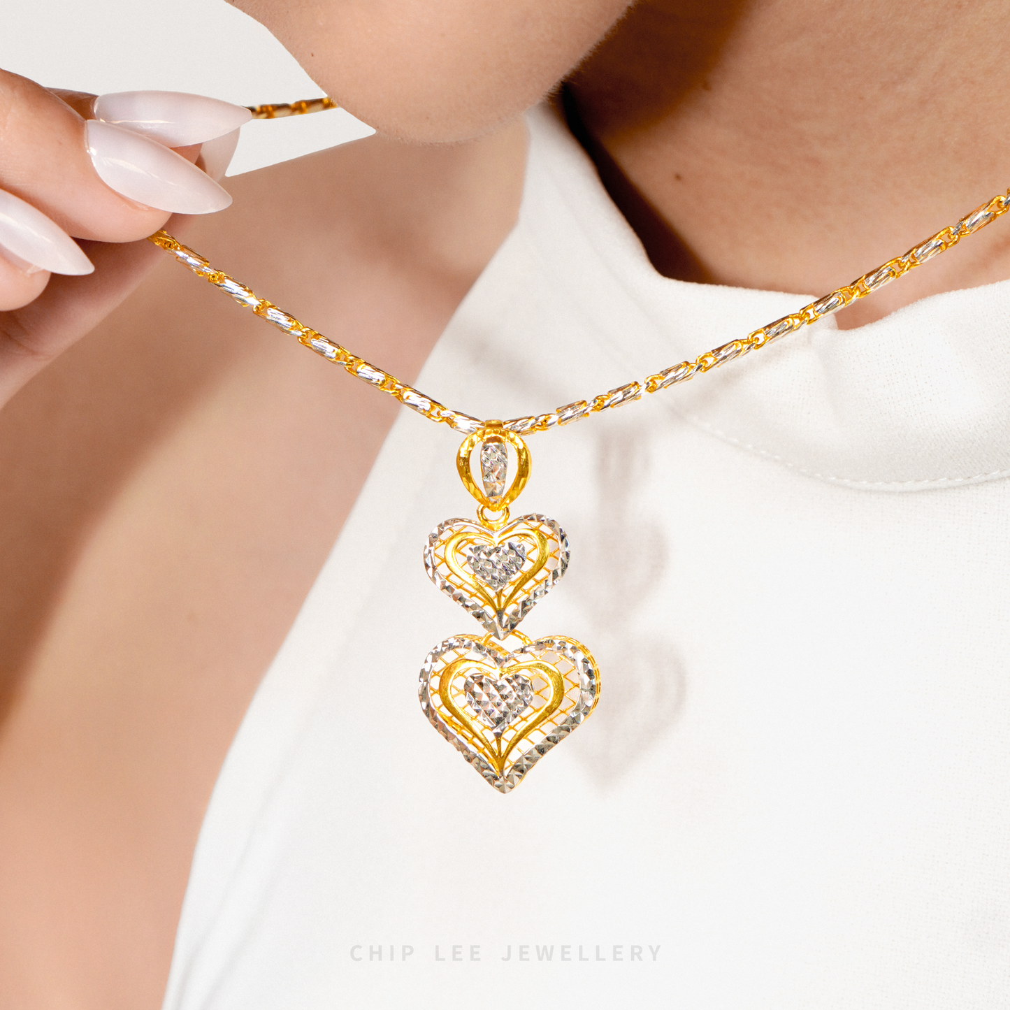 Close-up of a model wearing a 916 gold double heart pendant necklace, gently holding the chain against a white top.
