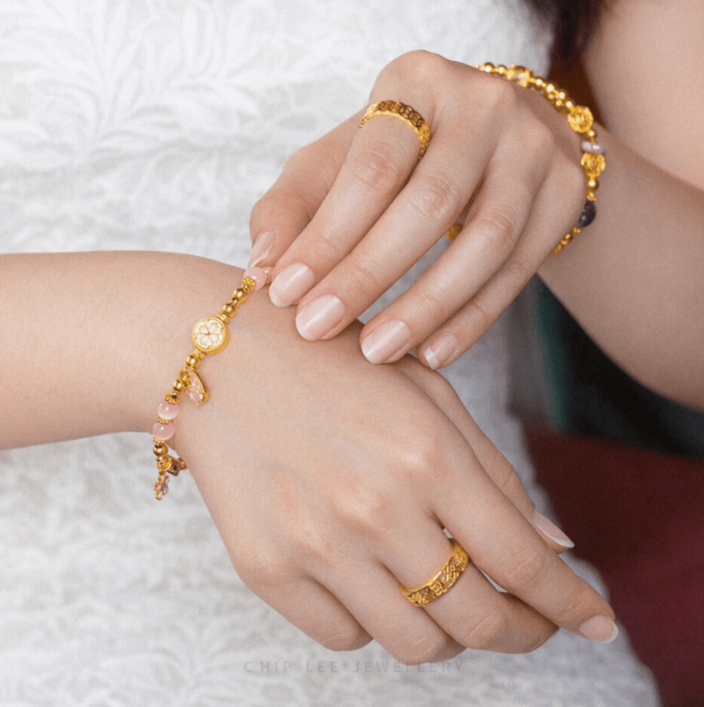 Close-up of hands adorned with 916 gold rings and delicate gold bracelets featuring pastel gemstone accents