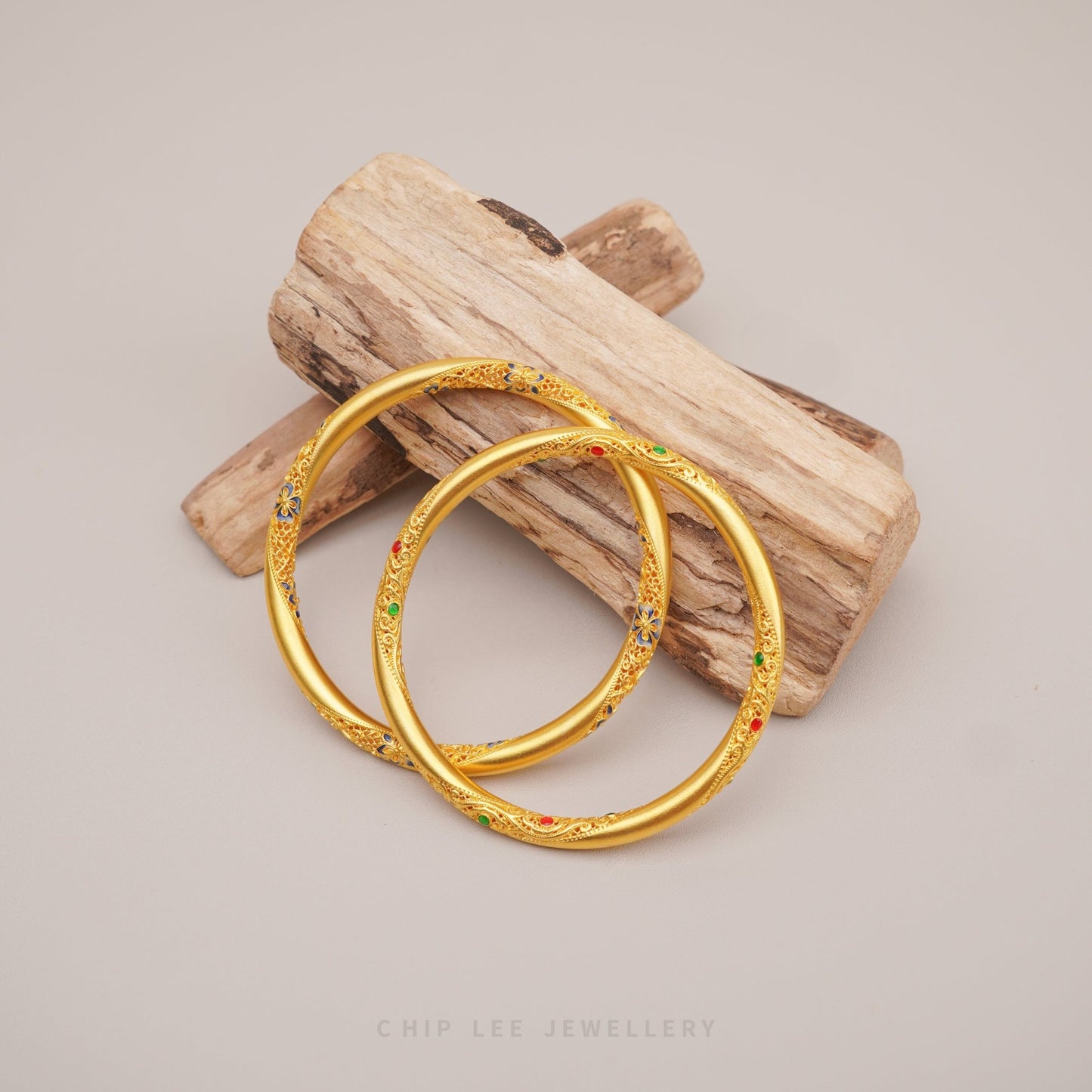 Gold bangles with colorful stones on a wooden block against a neutral background