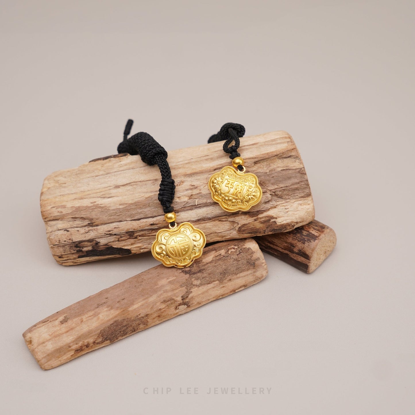 Gold pendants on black cords displayed on a wooden log with intricate and Chinese character designs.