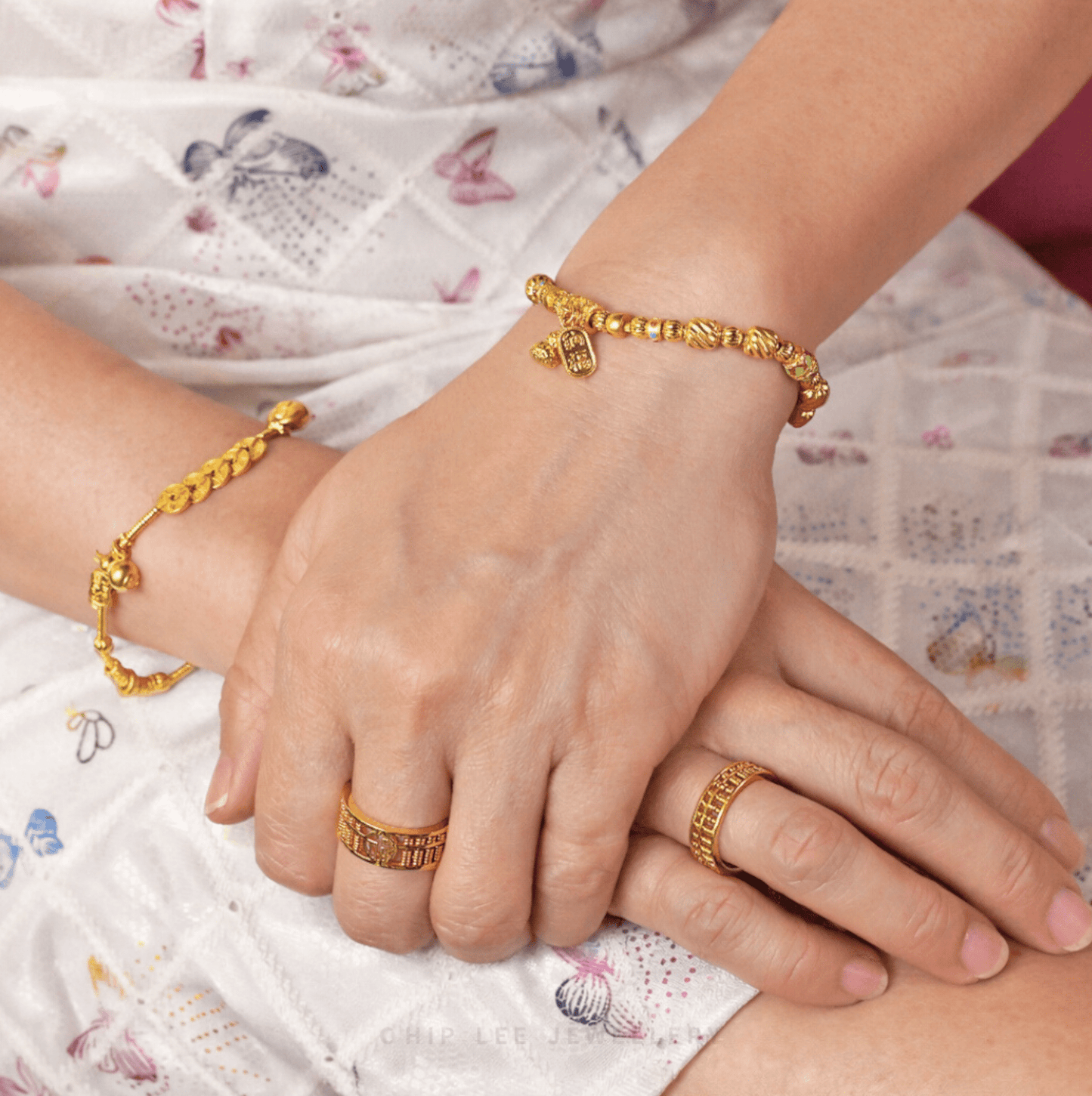 Close-up of hands adorned with matching 916 gold rings and bracelets, featuring intricate symbolic motifs