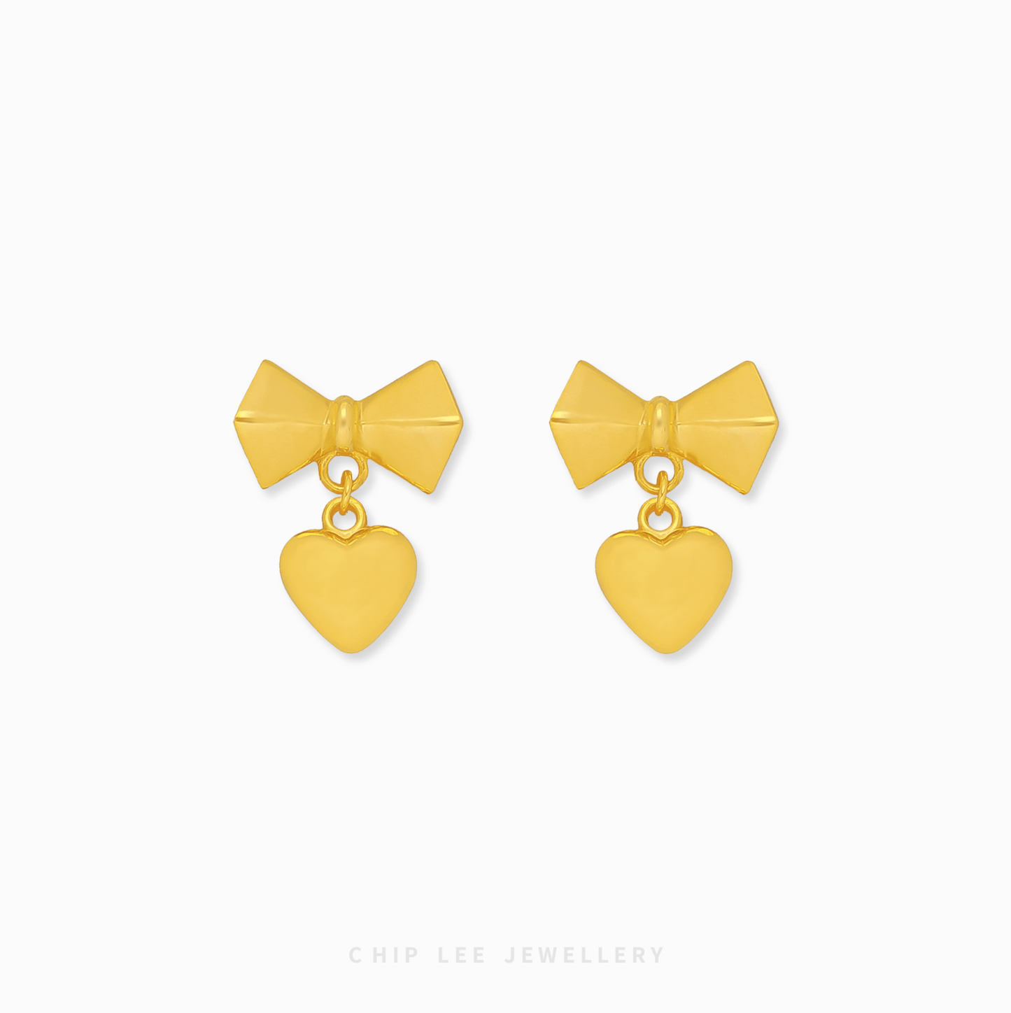 A pair of 999 pure gold bow dangling heart earrings showing the fluid movement and high polish of the 24K yellow gold on a dark background.