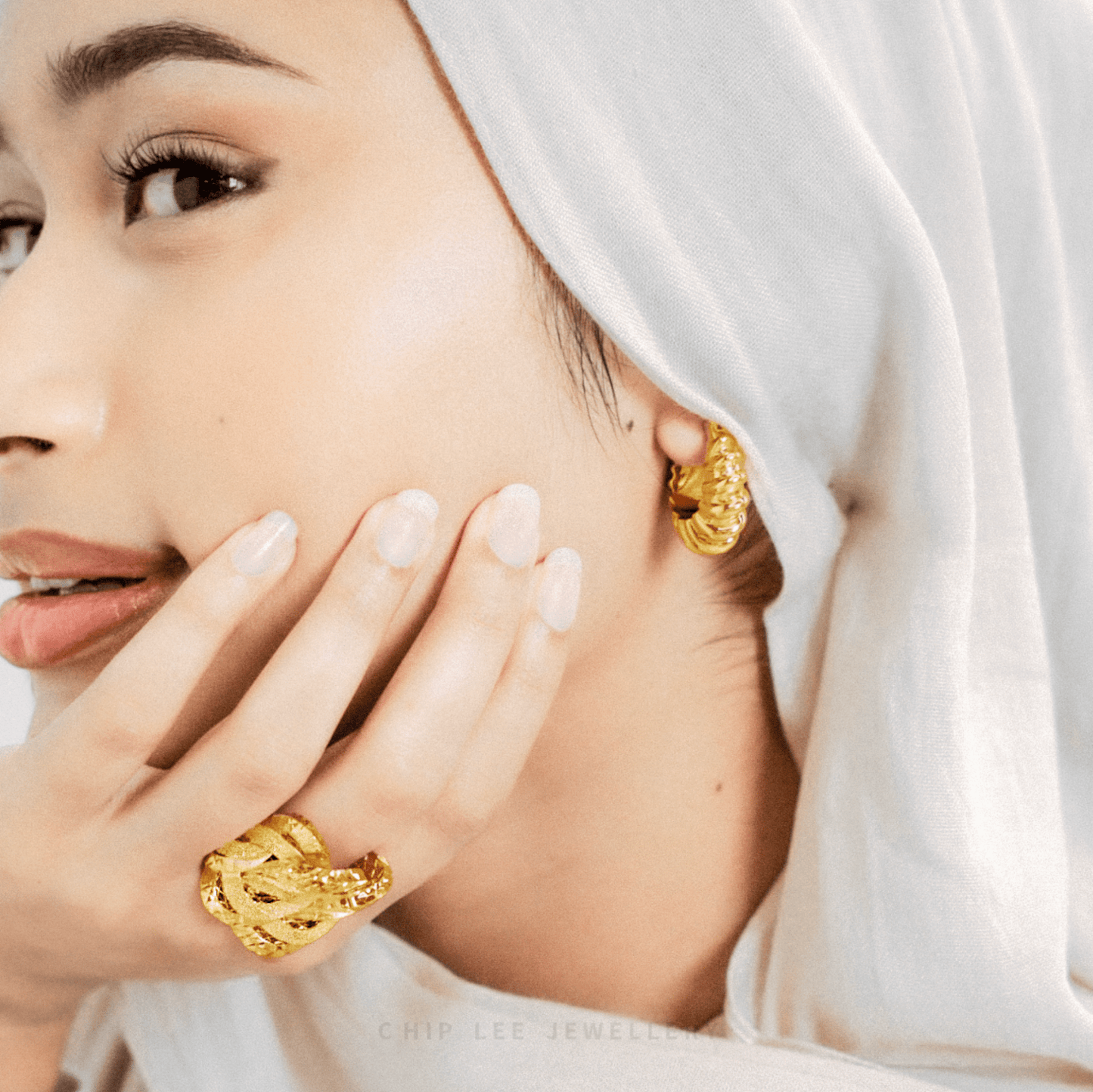 Woman wearing gold earrings and ring, with a soft focus on the jewellery.
