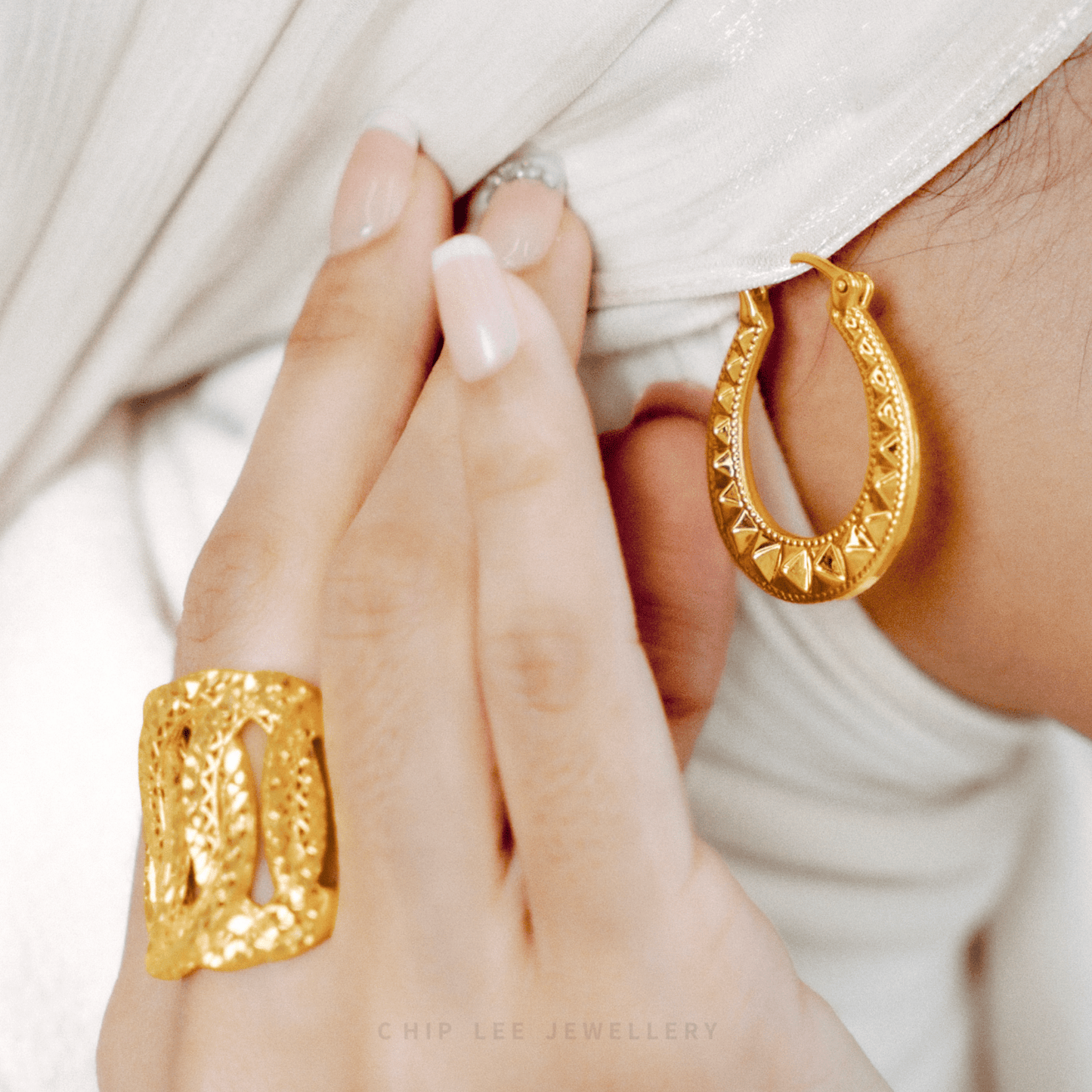 Gold hoop earrings and ring on a person's hand with a white background