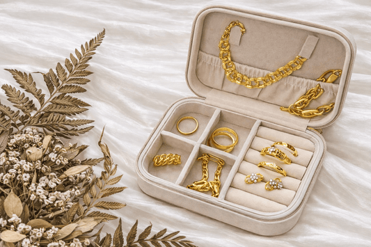 Flat lay of 916 and 999 gold jewellery displayed in a beige jewellery case, featuring gold rings, earrings, bracelet, and necklace on soft fabric background.