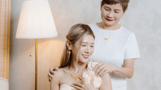 A candid, warm portrait features a young woman and an older woman standing close together, both wearing gold jewelry.