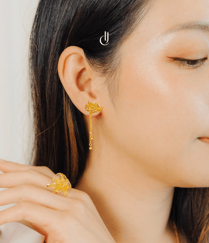 Close-up of a woman wearing gold floral earrings and a ring. Hallmarked in Singapore for certified purity and authenticity.