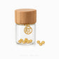 A clear glass jar with a light brown bamboo lid, featuring a gold-toned circular hanging charm and several small gold paw-shaped charms scattered at the base, on a white background.