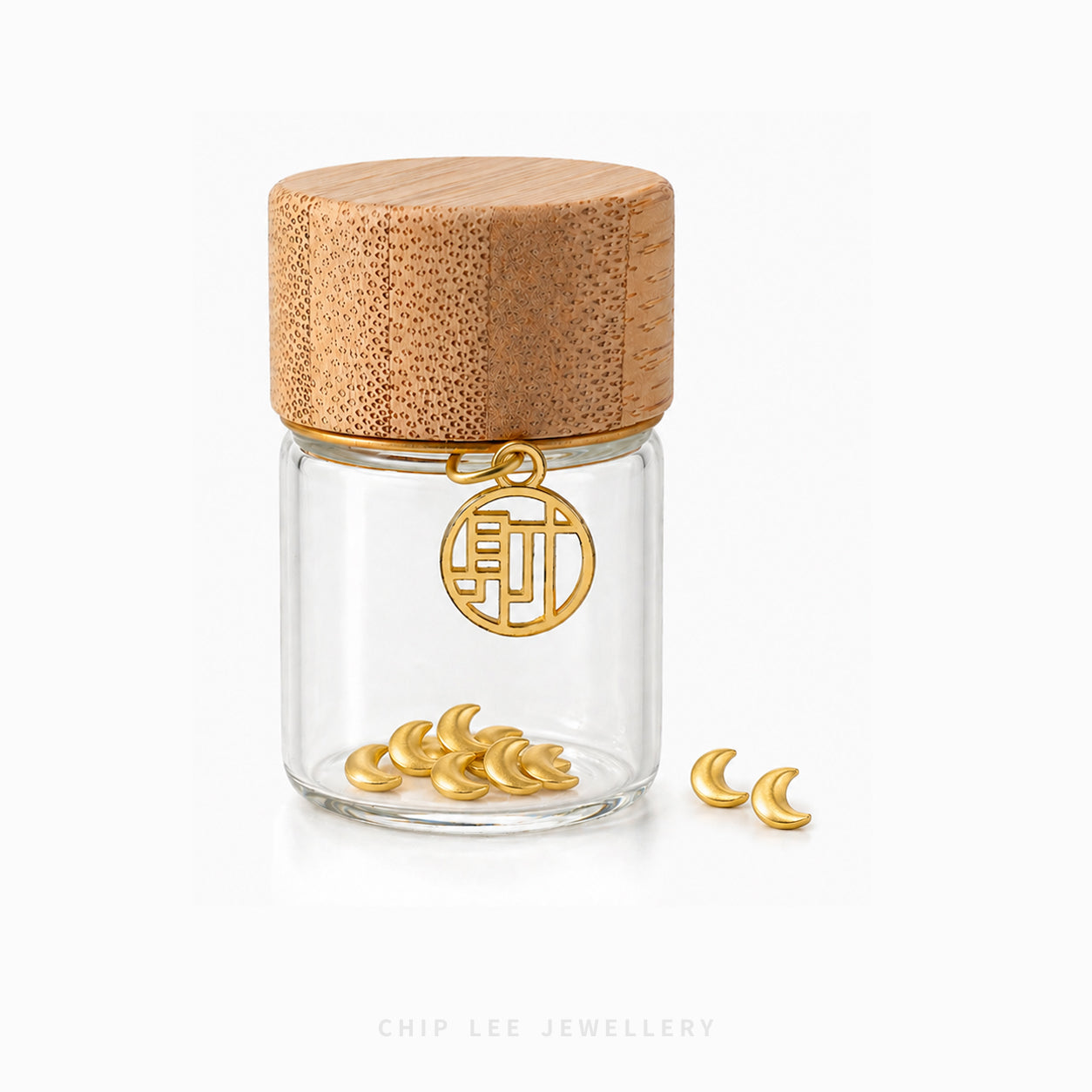 A clear glass jar with a light natural wood lid and a gold-tone hanging charm, shown on a white background with several small gold crescent moon charms placed beside it.