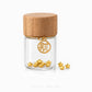 A small clear glass jar with a light wood lid and a gold-tone hanging charm, shown on a white background with several small gold star-shaped jewelry pieces beside it. The brand name 'CHIP LEE JEWELLERY' appears faintly at the bottom.