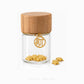 A small clear glass jar with a light wood lid and a gold-tone circular charm featuring a Chinese character, shown on a white background with small gold charms placed beside it. The brand name 'CHIP LEE JEWELLERY' appears faintly at the bottom.
