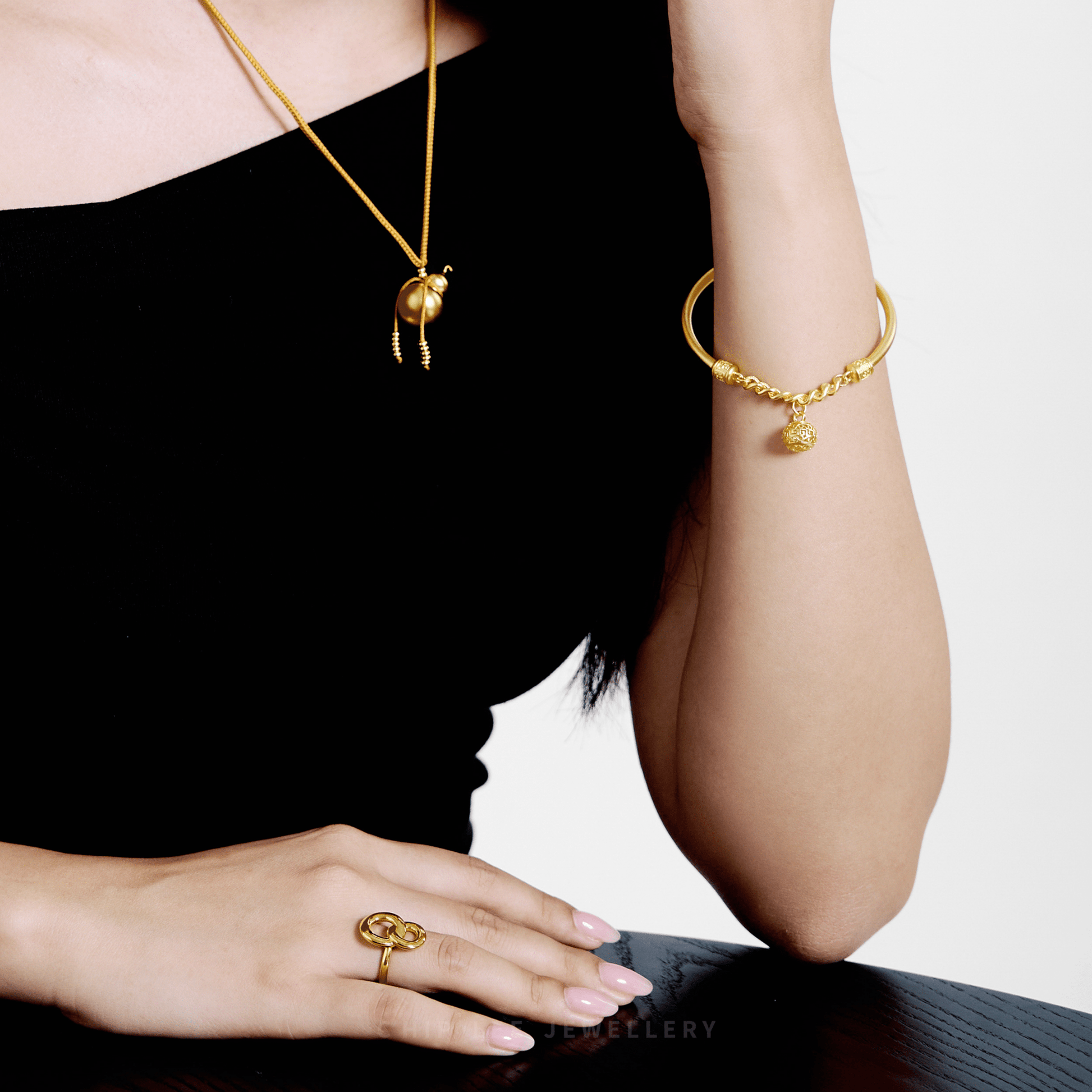 Gold jewelry including a necklace, bracelet, and ring on a person against a black background.