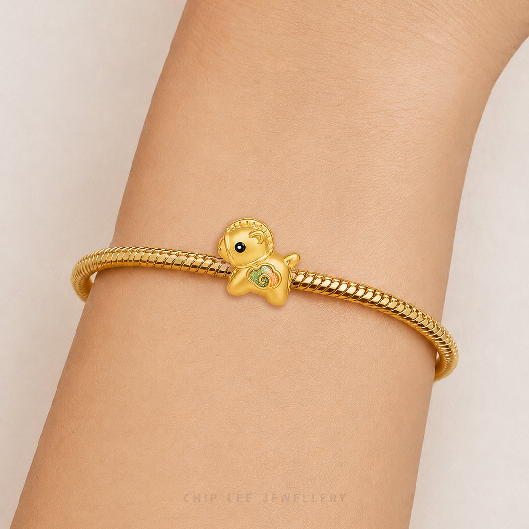 A gold snake-braided bracelet with a small duck charm featuring a green belly and black eye, shown worn on a person's wrist against a light beige background.