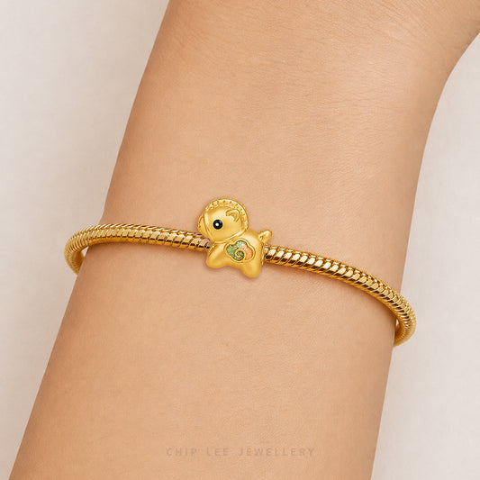 A gold snake-braided bracelet with a small duck charm featuring a green belly and black eye, shown worn on a person's wrist against a light beige background.