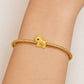 A gold snake-braided bracelet with a small duck charm featuring a green belly and black eye, shown worn on a person's wrist against a light beige background.