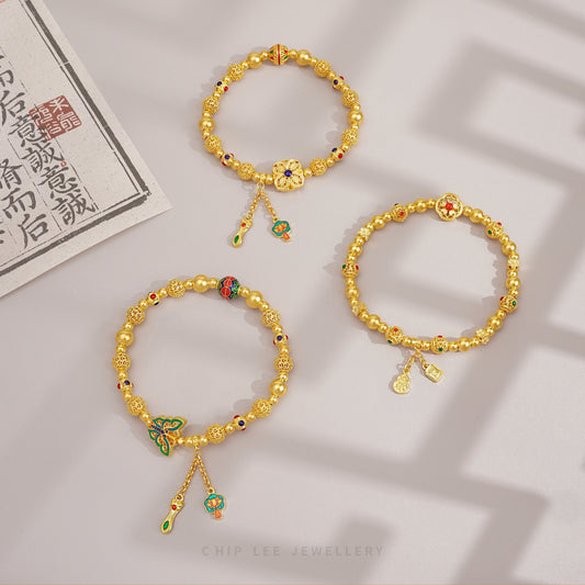 Three gold bracelets with colorful charms on a light brown background.