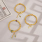 Three gold bracelets with colorful charms on a light brown background.