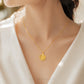 A delicate gold chain necklace with a small flower-shaped pendant worn by a model in a white V-neck top. The pendant features a sunburst design with a central circular detail.