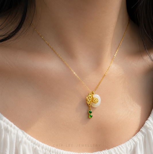 Gold pendant with green gemstones and white jade on a white background