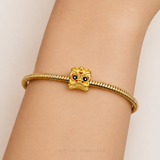 A gold-plated snake-braided bracelet with a lion head charm featuring red and black enamel details, shown worn on a person's wrist.