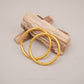 Gold bangles with colorful stones on a wooden block against a neutral background