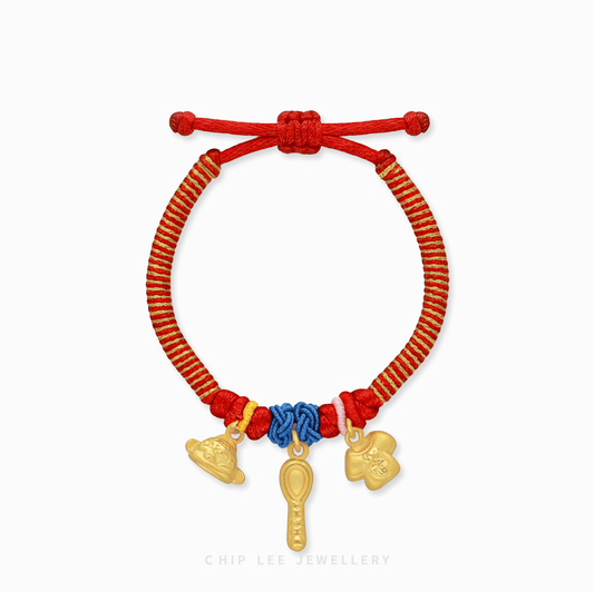 A detailed close-up of a 999 Pure Gold Adjustable Baby Bracelet, showcasing the Hat, Spoon, and Shirt charms on a red thread