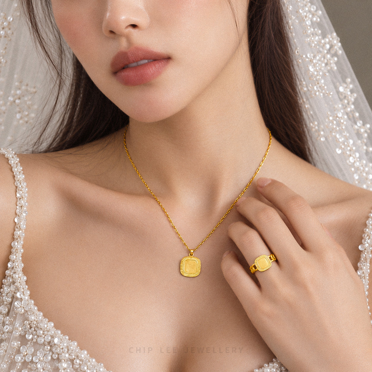 A close-up lifestyle shot of a model wearing a gold pendant necklace and a matching gold ring, dressed in a white beaded bridal gown and veil. The brand name 'CHIP LEE JEWELLERY' is subtly visible at the bottom.