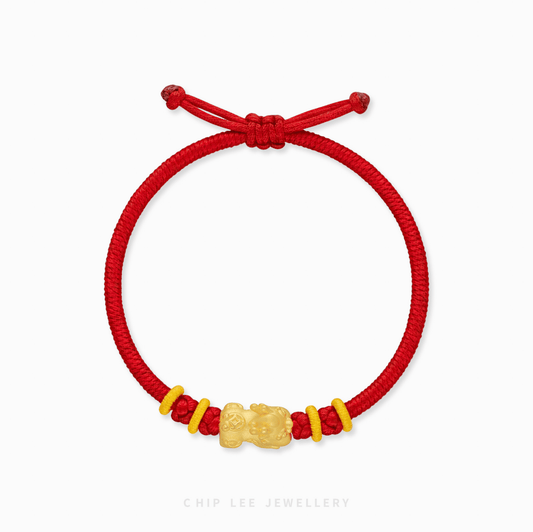 A close-up of a 999 Pure Gold Pixiu Adjustable Baby Bracelet, showing the detailed gold charm on a vibrant red string.