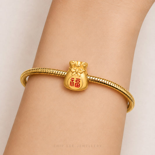 A gold snake-braided bracelet with a small gold pouch charm featuring a red Chinese character for good fortune, shown worn on a person's wrist.
