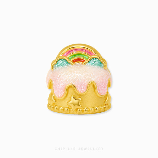 A gold crown-shaped charm designed to look like a frosted cake, featuring pink glittery icing, a small gold star, and a colorful rainbow on top, shown on a plain white background with 'CHIP LEE JEWELLERY' text at the bottom.