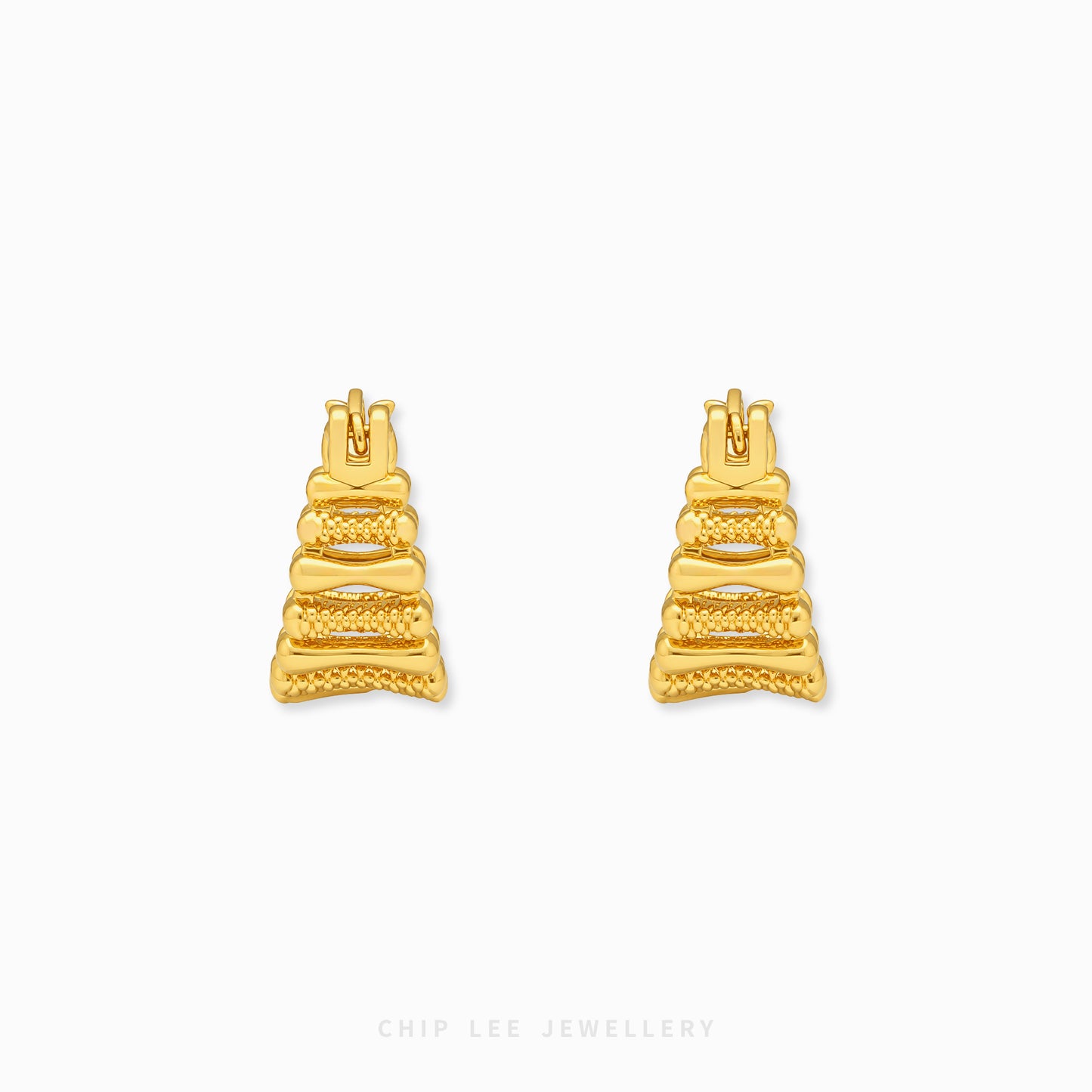 A pair of gold geometric stud earrings with a textured, tiered design, displayed on a clean white background with a subtle brand watermark at the bottom.