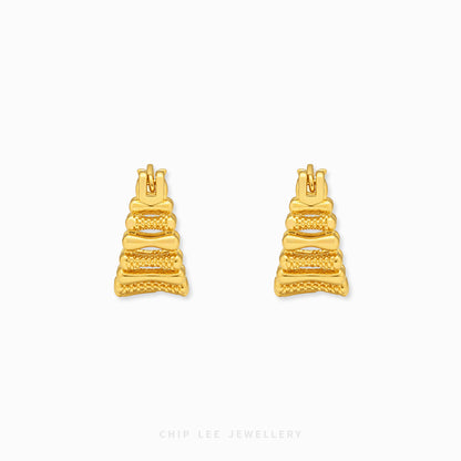 A pair of gold geometric stud earrings with a textured, tiered design, displayed on a clean white background with a subtle brand watermark at the bottom.