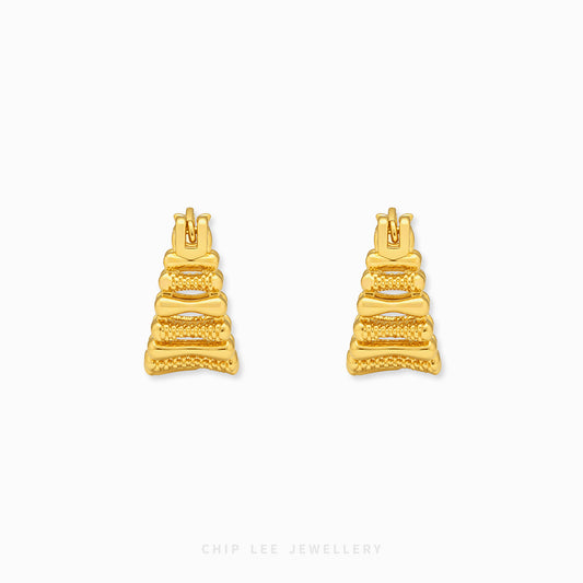 A pair of gold geometric stud earrings with a textured, tiered design, displayed on a clean white background with a subtle brand watermark at the bottom.