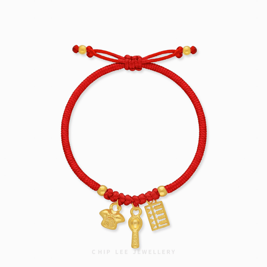 A detailed close-up of a 999 Pure Gold Adjustable Baby Bracelet, showcasing the Shirt, Spoon, and Abacus charms on a red string.