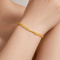 A delicate gold bangle bracelet with a twisted, textured design, shown worn on a person's wrist. The background consists of soft-focus skin tones.