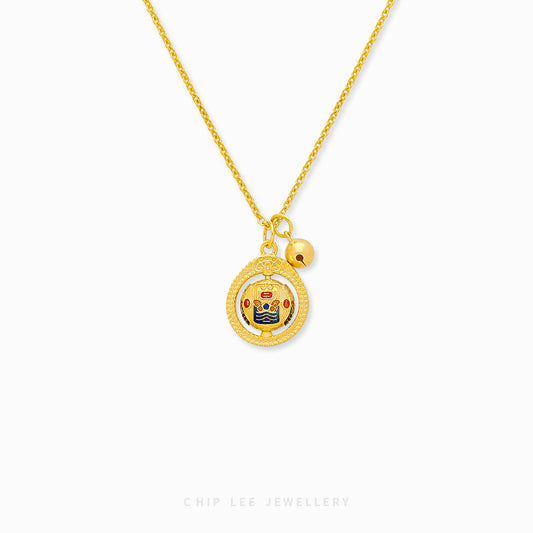 A gold necklace with a circular spinning charm pendant in the center, featuring intricate designs, and a small gold bell on the end of the chain.