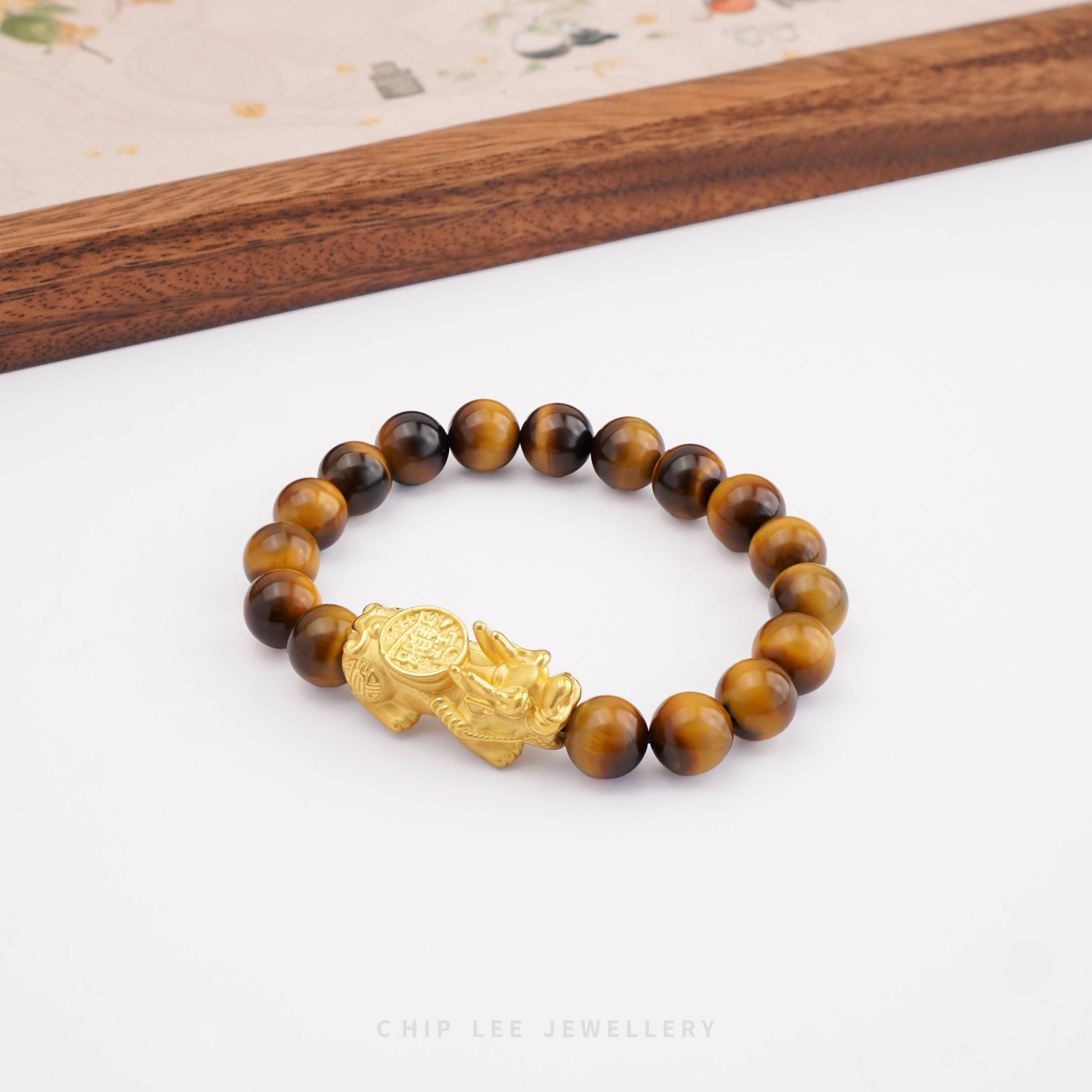 Close-up of 999 Pure Gold 招财纳福 Tiger Eye Pixiu Bracelet featuring a gold Pixiu charm and tiger eye beads on display.