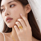 A close-up lifestyle shot of a model wearing a gold necklace and matching gold ring with a leaf motif. The jewelry features intricate filigree and textured details, presented on a model in a bridal-style white dress with a veil.