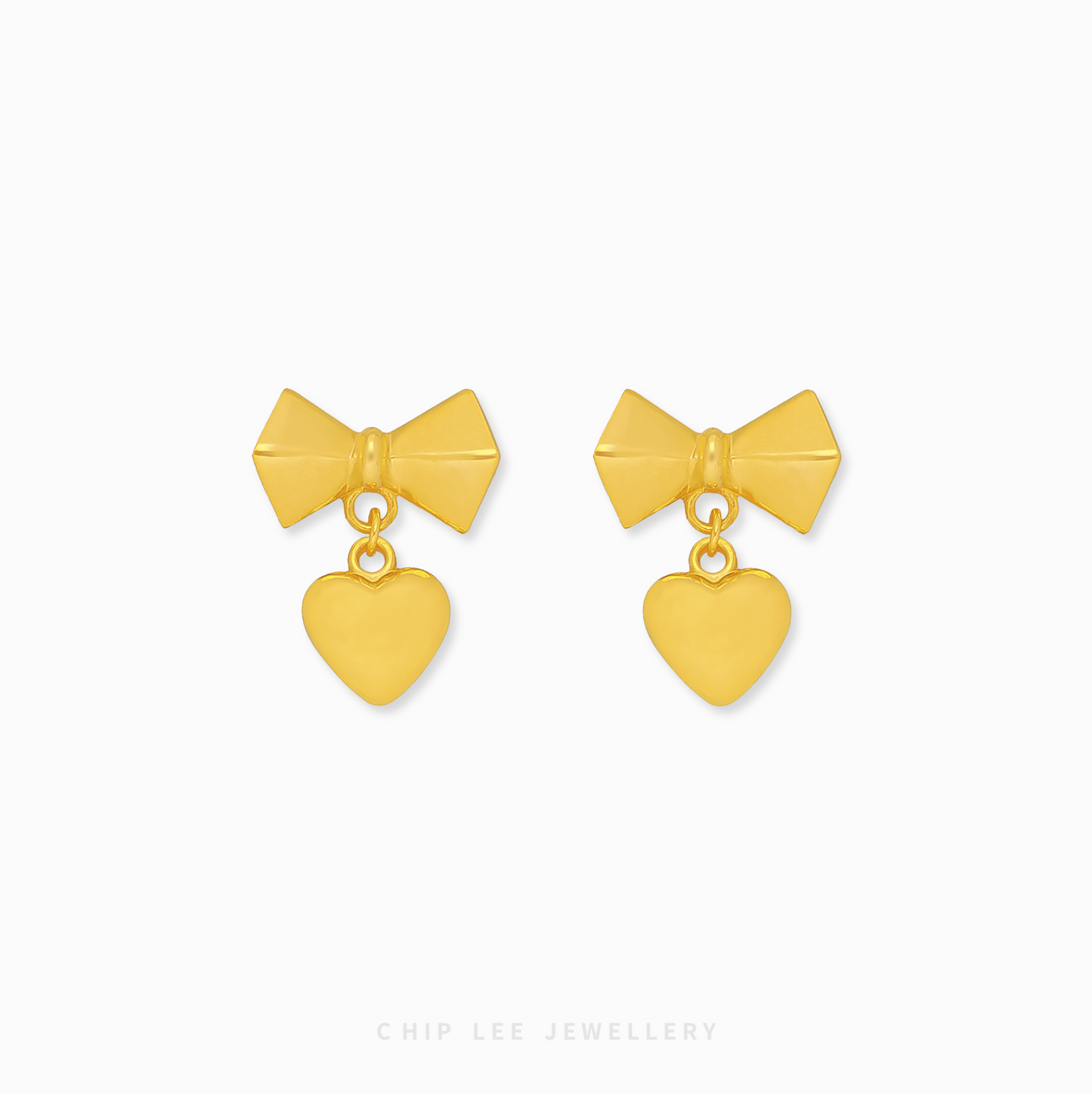 A pair of 999 pure gold bow dangling heart earrings showing the fluid movement and high polish of the 24K yellow gold on a dark background.

