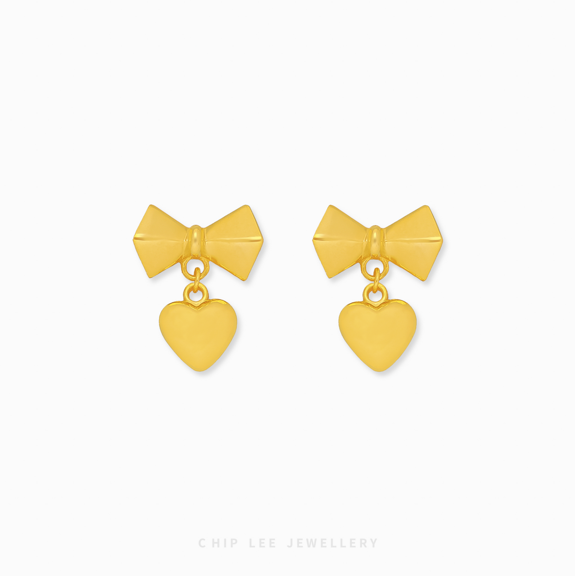 A pair of 999 pure gold bow dangling heart earrings showing the fluid movement and high polish of the 24K yellow gold on a dark background.

