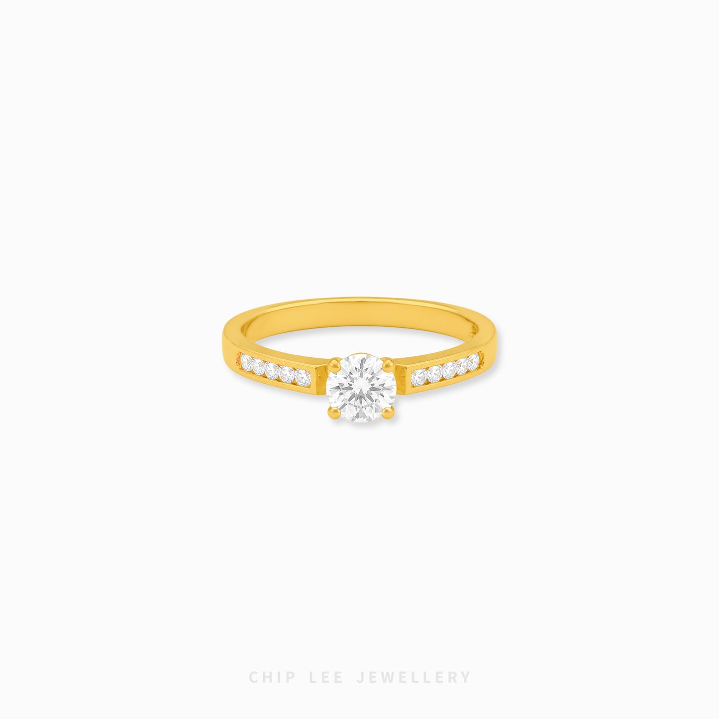 A yellow gold solitaire engagement ring with a round-cut center stone and a row of small pavé-set stones along the band, shown on a light gray background with Chip Lee Jewellery branding at the bottom.