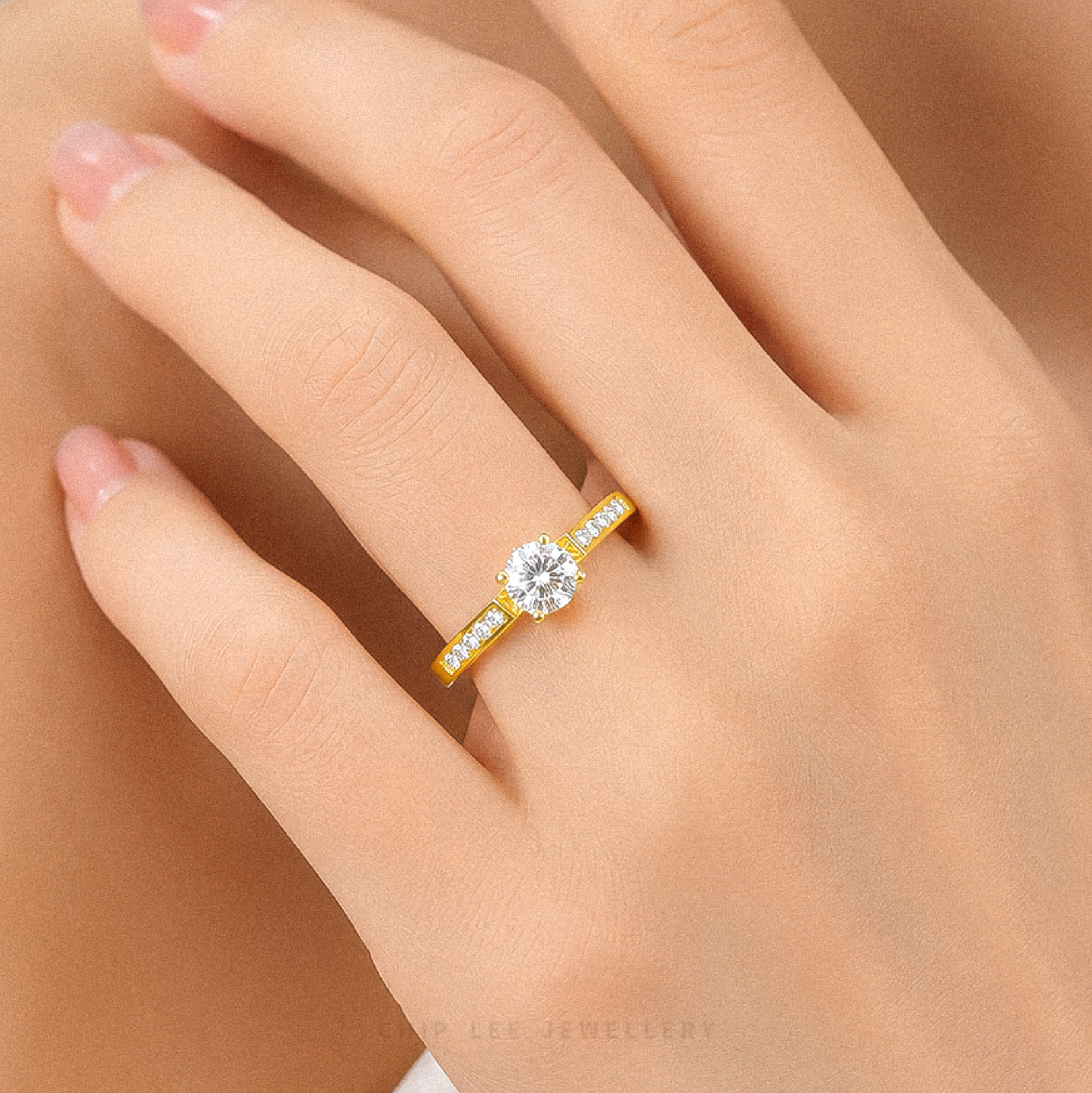 A yellow gold solitaire engagement ring with a round-cut clear center stone and small side stones, shown worn on a hand.