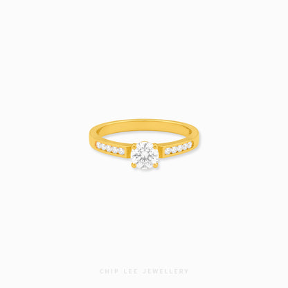 A yellow gold solitaire engagement ring with a round-cut center stone and a row of small pavé-set stones along the band, shown on a light gray background with Chip Lee Jewellery branding at the bottom.