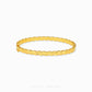A polished yellow gold bangle bracelet with a textured, ridged outer surface and a smooth inner band, displayed on a clean white background with a brand watermark at the bottom.