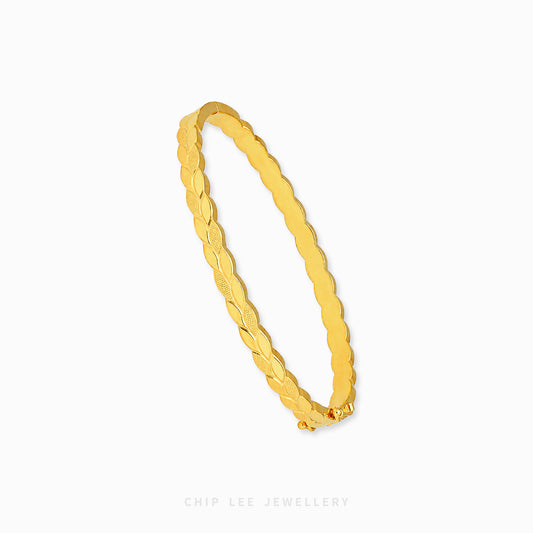 A gold bangle bracelet with a textured, ridged pattern, shown on a clean white background with a brand watermark at the bottom.