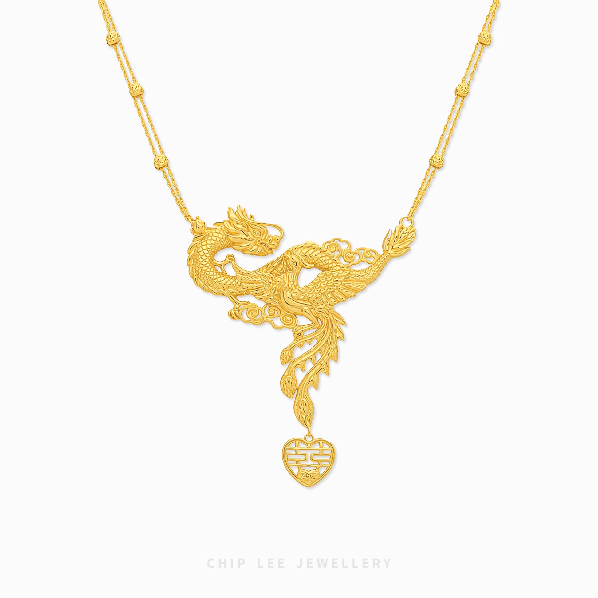 ntricately designed gold necklace featuring a mythical phoenix-dragon pendant with flowing feather and scale details, suspended on a delicate decorative chain with a dangling heart-shaped charm against a light background.
