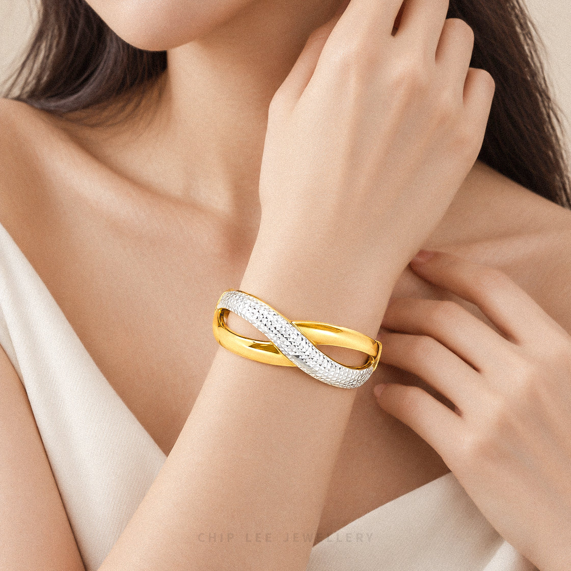 A close-up lifestyle shot of a model wearing a double-band bangle bracelet by Chip Lee Jewellery. The bracelet features one polished yellow gold band and one pavé-set white metal band.