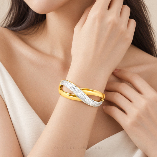 A close-up lifestyle shot of a model wearing a double-band bangle bracelet by Chip Lee Jewellery. The bracelet features one polished yellow gold band and one pavé-set white metal band.