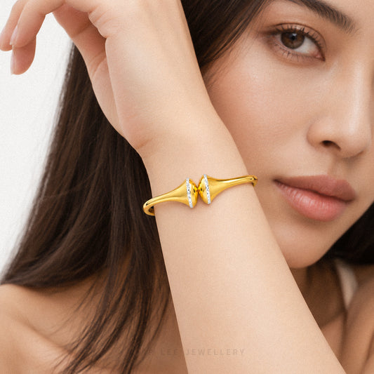 A close-up lifestyle shot of a model wearing a gold butterfly cuff bracelet with clear crystal accents. The model's face and hand are visible against a clean, light background.