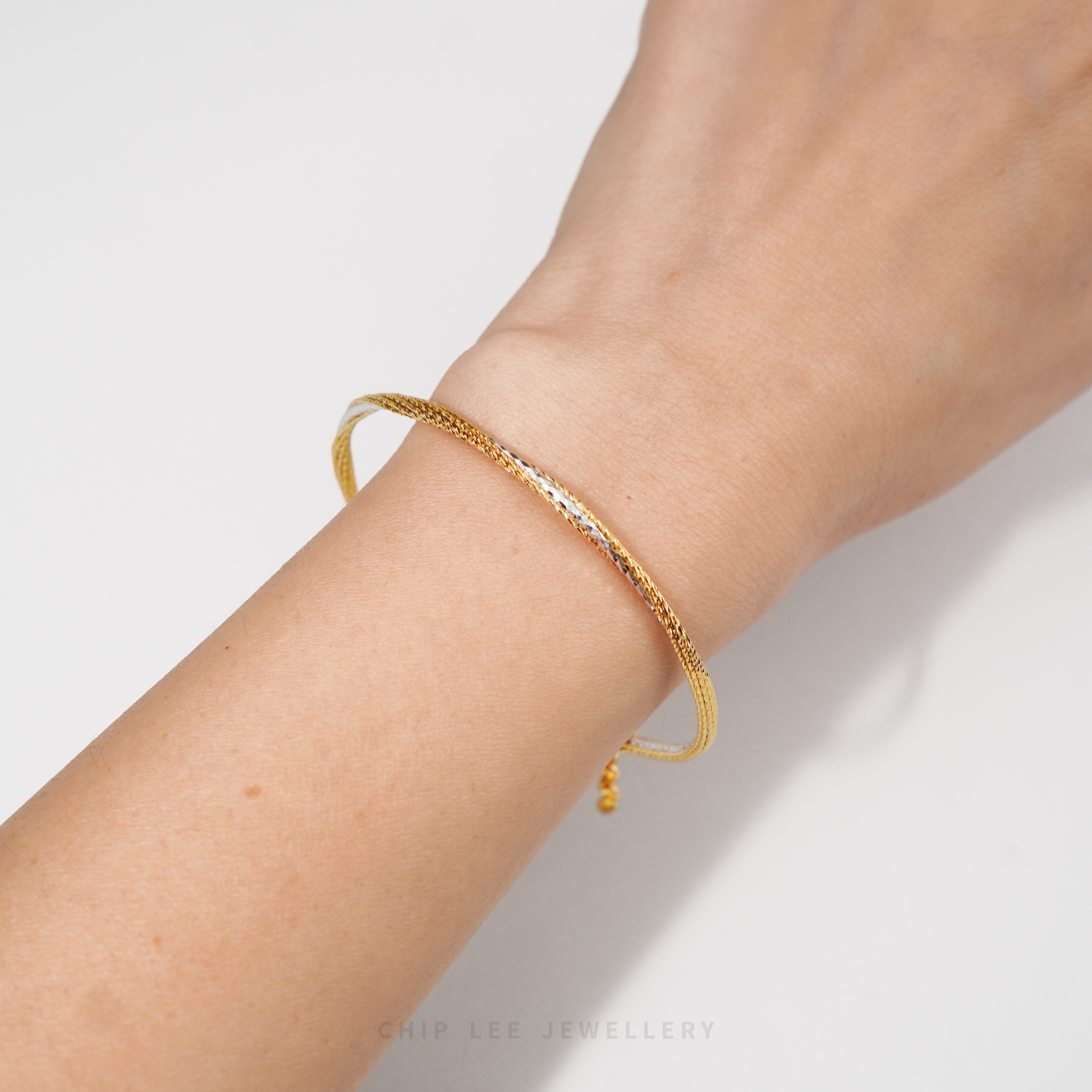 A gold textured bangle bracelet with a small dangling bead, shown worn on a person's wrist against a clean white background.